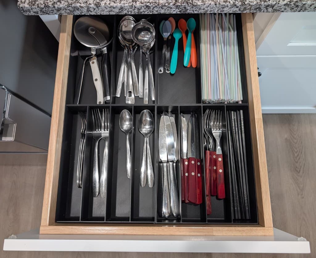 Custom black getGridded divider organizing utensils in a kitchen drawer